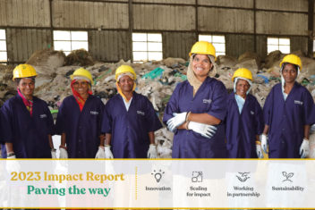 A row of women wearing blue FINILOOP waste worker uniforms with a yellow hardhat. Banner across the photo reading Impact Report 2023 - Paving the way