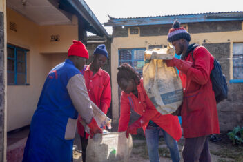 Three people in red uniforms and one person in blue uniform putting waste into a large sack