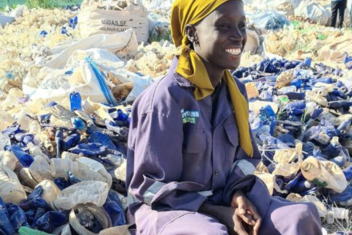 Smiling waste worker sat on bucket with a yellow headscarf and blue uniform