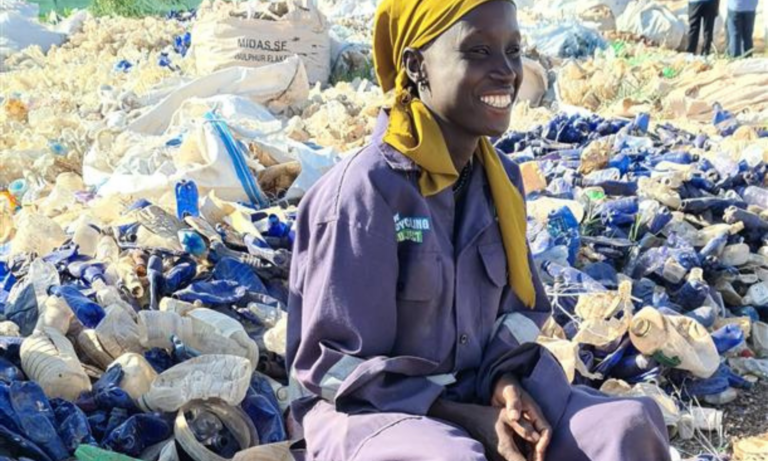 Smiling waste worker sat on bucket with a yellow headscarf and blue uniform