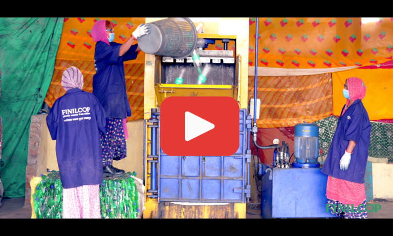 Play icon overlaying a picture of three women in blue safety coats loading plastic into a baling machine